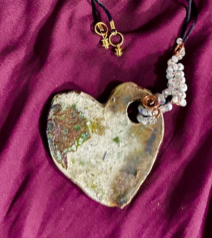 Have A Heart ! Each heart pendant is handmade with love! It is 3"x 3" and weighs approx. 3ozs. This pendant has a toasty white copper metallic raku glazes that renders a unique translucent patina. The heart has a textured pattern . Both sides are are different and equally beautiful! It holds a spiral of white mini beads on a spiral copper wire. This pendant has a nice 12" black rattail cord!