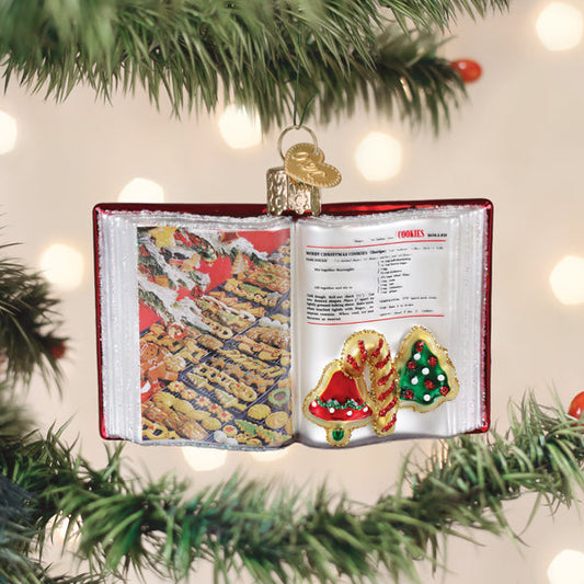 Old World Christmas Betty Crocker Cookbook glass ornament hanging on a Christmas tree, designed as an open cookbook with a holiday cookie recipe and decorated cookies on the pages.