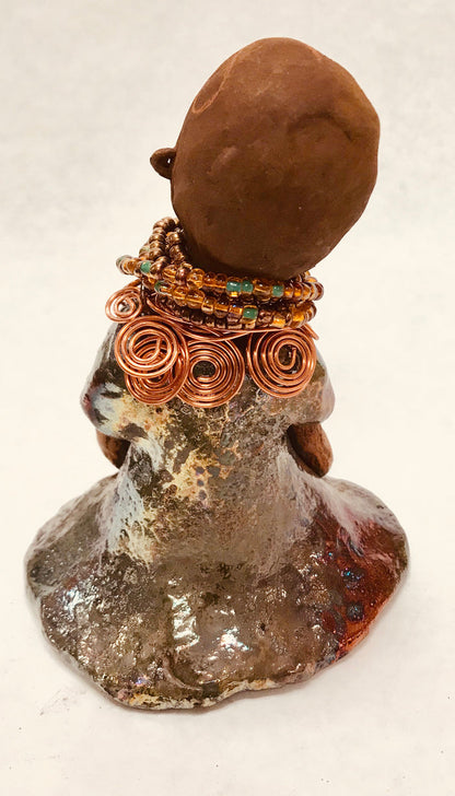 Meet Faye! Faye stands 7" x 5" x 4" and weighs 2.3 lbs. She has a lovely two tone honey brown complexion with  chocolate brown lips. She has a braided hairstyle.  Faye has a colorful metallic green antique glazed dress. She wears an awesome beaded collar with a copper spiral necklace. Her long loving arms rest at her side. With eyes wide opened, Faye has hopes of finding a new home.