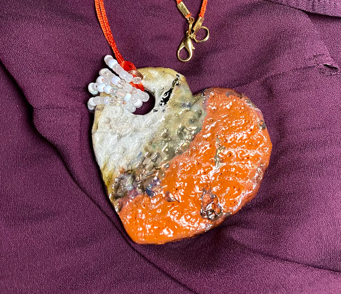 Have A Heart ! Each heart pendant is handmade with love! It is 3"x 3"and weighs approx. 3ozs. This pendant has a red violet and gold metallic raku glazes that renders a unique translucent  patina. The heart has a textured pattern . Both sides are  are different and equally beautiful! It holds a spiral of white and clear mini beads on a spiral copper wire. This pendant has a nice 12" red suede cord!