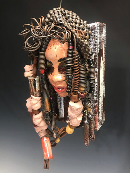 Kamara is uniquely mounted on a painted 6"x 4"x 2" canvas. It weighs 1.6lbs.     Her face is formed with hand coiled wire, raku beads, textured brown cloth, and multi color raku beads.     Kamara's face beams with pale pink crackle glaze and ruby red lips.  Kamara is ready to be hung in a special place!