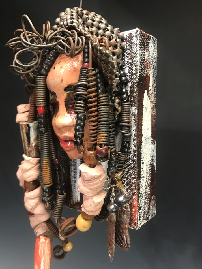 Kamara is uniquely mounted on a painted 6"x 4"x 2" canvas. It weighs 1.6lbs.     Her face is formed with hand coiled wire, raku beads, textured brown cloth, and multi color raku beads.     Kamara's face beams with pale pink crackle glaze and ruby red lips.  Kamara is ready to be hung in a special place!