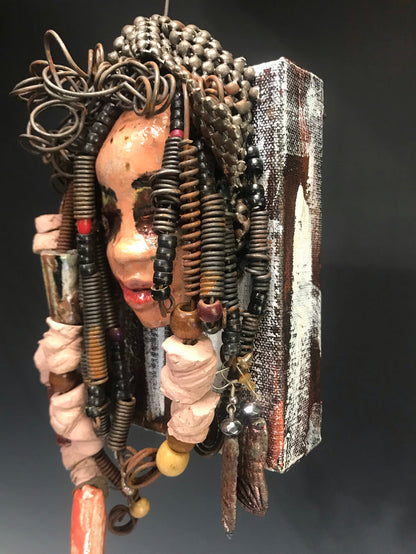 Kamara is uniquely mounted on a painted 6"x 4"x 2" canvas. It weighs 1.6lbs.     Her face is formed with hand coiled wire, raku beads, textured brown cloth, and multi color raku beads.     Kamara's face beams with pale pink crackle glaze and ruby red lips.  Kamara is ready to be hung in a special place!