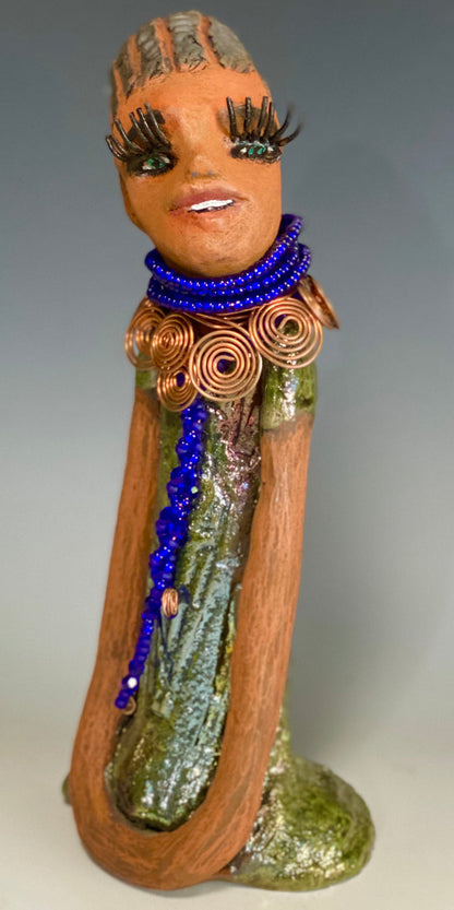 Meet Ophelia! Ophelia stands 7.5" x 4" x 5" and weighs 1.02  lbs. She has a lovely honey brown complexion with reddish brown lips. She has a short braided hairstyle.  Ophelia has a colorful metallic antique copper glazed dress. She wears spiral copper wire necklaces on top of an aqua blue beaded collar. Ophelia long loving arms rest at her side. With accent blue eye shadow and eyes wide opened, Ophelia has hopes of finding  her way into your home!