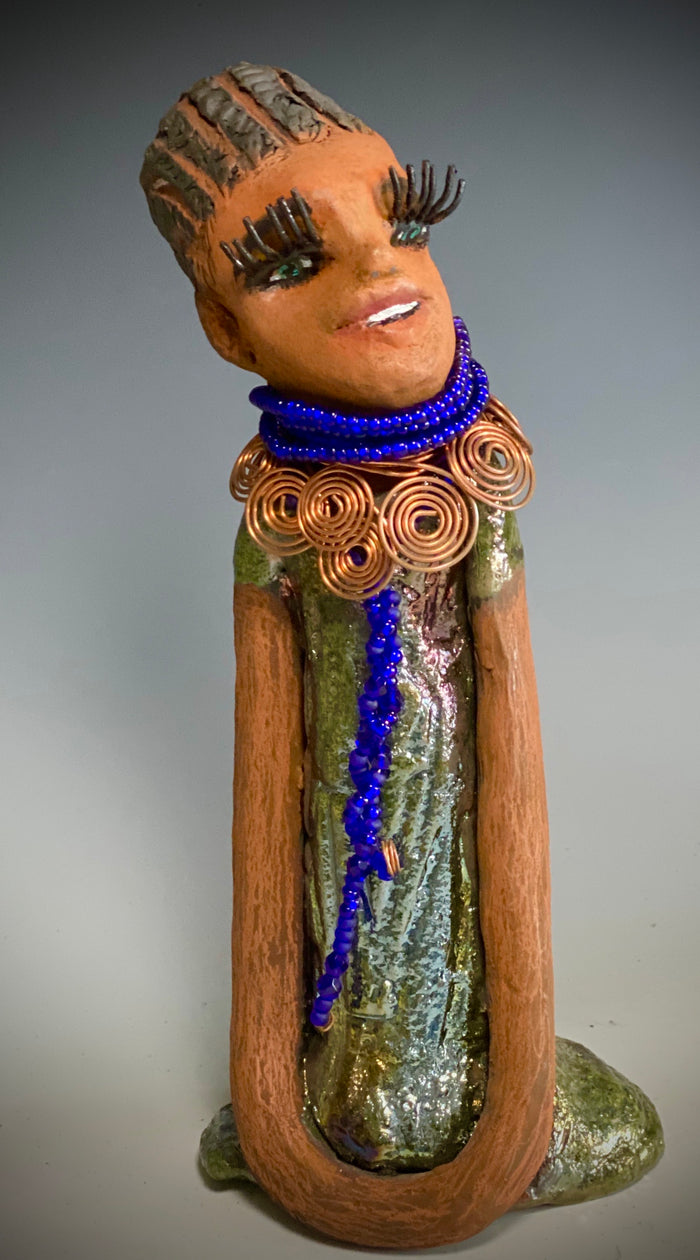 Meet Ophelia! Ophelia stands 7.5" x 4" x 5" and weighs 1.02  lbs. She has a lovely honey brown complexion with reddish brown lips. She has a short braided hairstyle.  Ophelia has a colorful metallic antique copper glazed dress. She wears spiral copper wire necklaces on top of an aqua blue beaded collar. Ophelia long loving arms rest at her side. With accent blue eye shadow and eyes wide opened, Ophelia has hopes of finding  her way into your home!