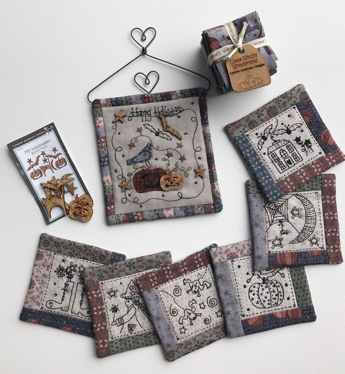 A collection of fabric pieces with various spooky and Halloween-themed designs, such as pumpkins and owls, intended for crafting a mini quilt.
