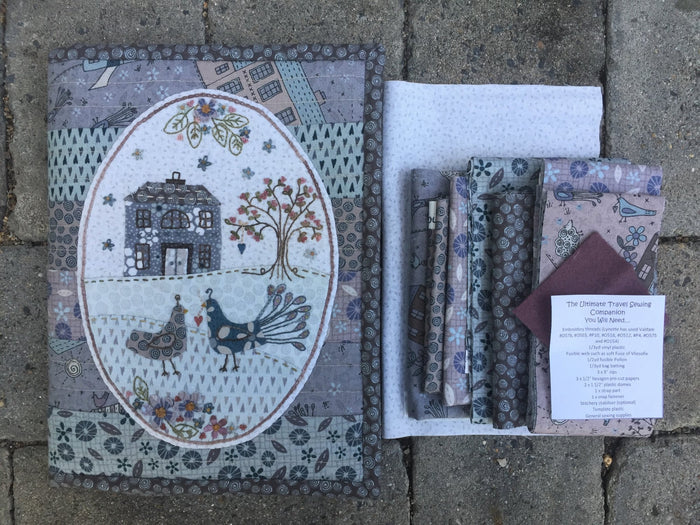 A travel sewing companion kit laid out on a tiled surface, including a colorful fabric with applique design, a set of embroidery threads, zips, and other sewing materials.