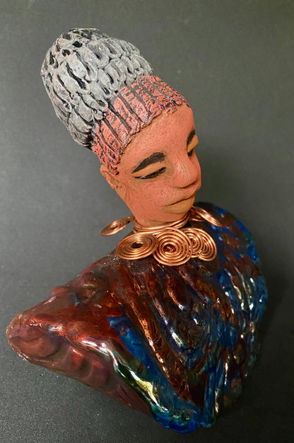 Meet Tia! Tia looks up with joy and anticipation! Tia stands 7" x 6" x 4" and weighs 1.90 lbs. She has a beautiful textured copper and blue robe. Tia has braided clay hair up in a bun. She has a honey brown complexion and soft light brown lips. Tia will make for great conversation in your home.  Free Shipping! Check out our Shipping and Return policy