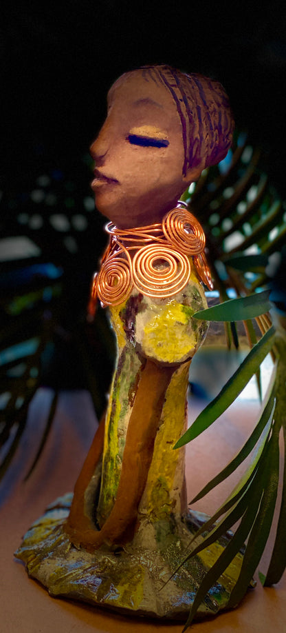 Meet Trisha! Trisha stands 9.5" x 5”x 5" and weighs  1.3 lbs.  Trisha has a lovely glossy yellow  green dress with a copper spiral necklace.   Her hair is etched in clay. Her long arms rest at her side. Trisha is at a special low price. This makes her an excellent starter piece from the Herdew Collection!